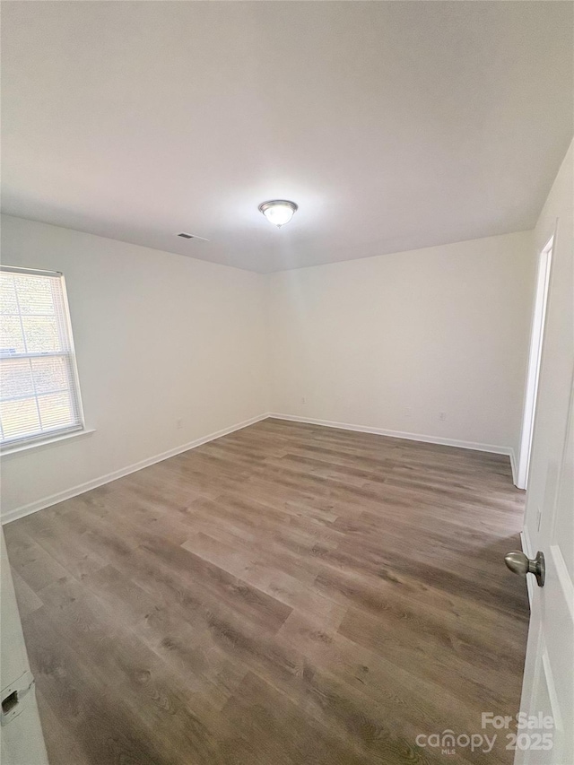 spare room featuring visible vents, baseboards, and wood finished floors