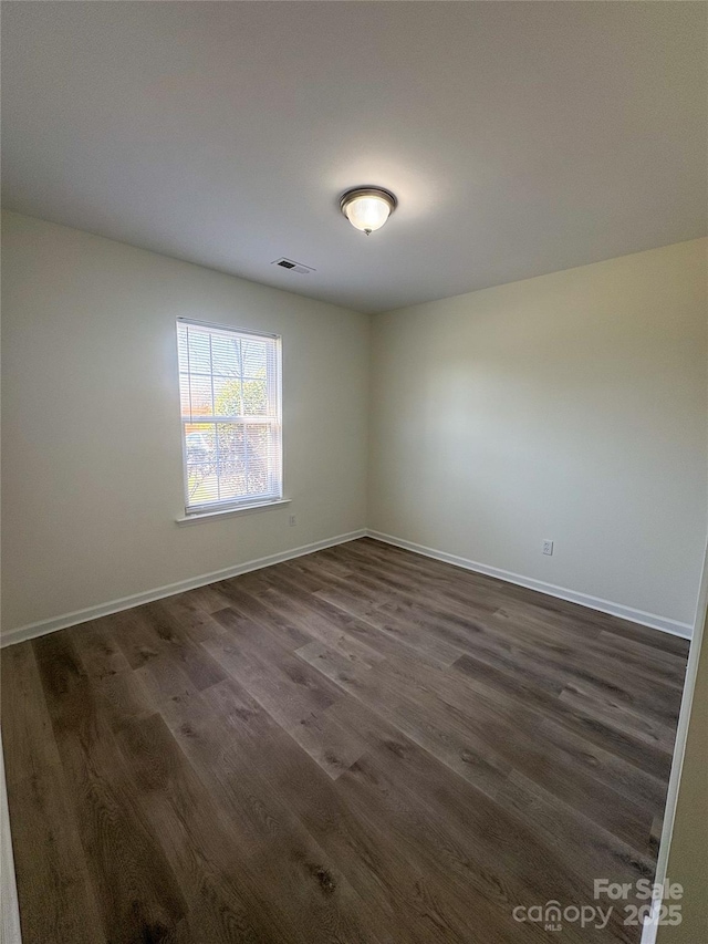 unfurnished room featuring baseboards, dark wood-style floors, and visible vents