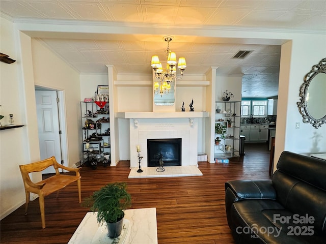 living room with a fireplace with raised hearth, wood finished floors, visible vents, and a notable chandelier