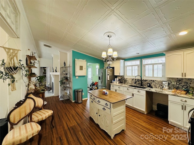 kitchen featuring dark wood-style flooring, stainless steel refrigerator with ice dispenser, a sink, and an ornate ceiling