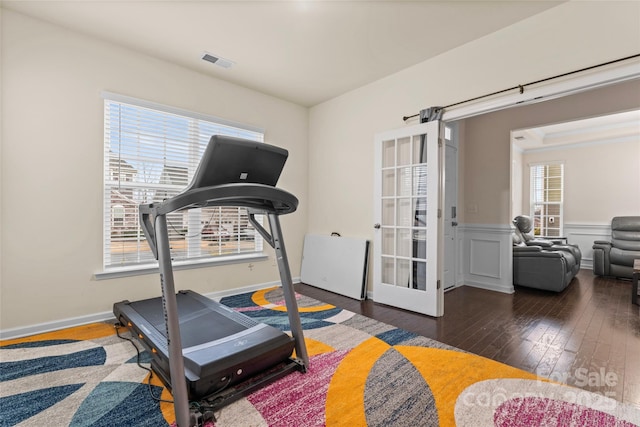 workout area featuring wainscoting, visible vents, a healthy amount of sunlight, and wood-type flooring