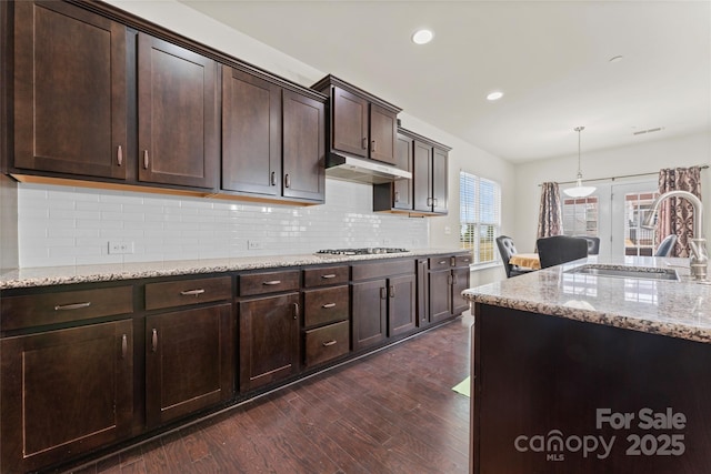 kitchen with light stone countertops, dark wood-style floors, a sink, dark brown cabinetry, and under cabinet range hood