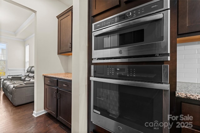 kitchen featuring light stone countertops, dark wood-style flooring, ornamental molding, dark brown cabinetry, and backsplash