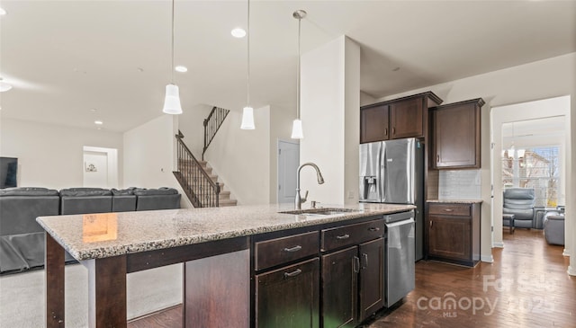 kitchen featuring light stone countertops, a sink, dark brown cabinets, appliances with stainless steel finishes, and open floor plan