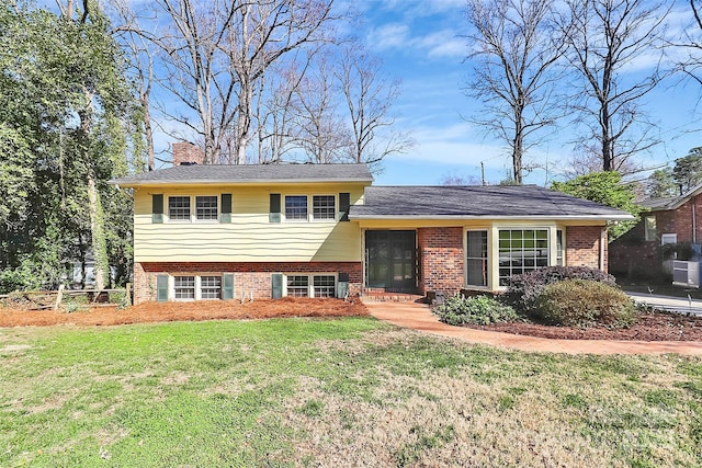 tri-level home with brick siding, a chimney, and a front yard