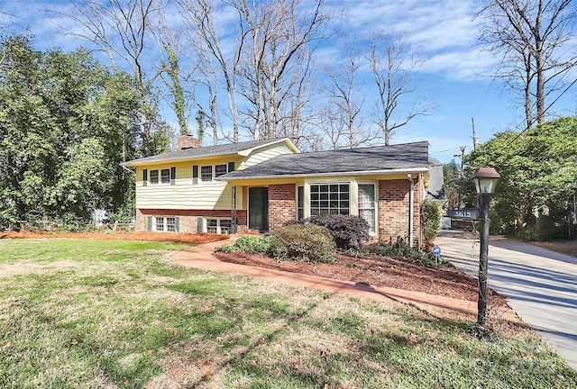 tri-level home featuring brick siding, a chimney, and a front lawn