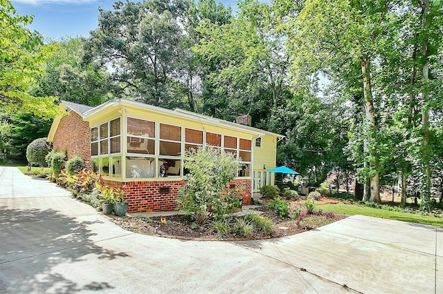 exterior space with brick siding, a chimney, and a sunroom