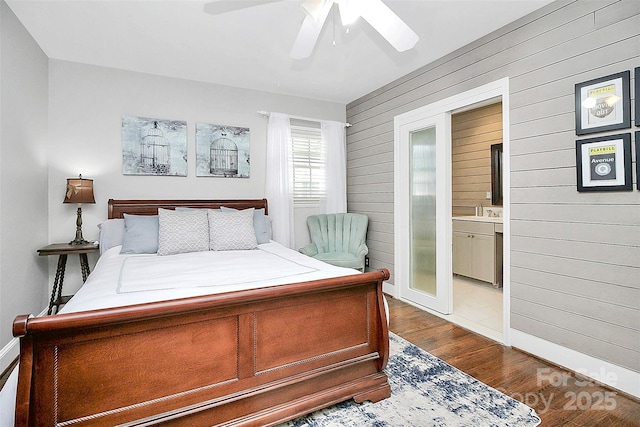 bedroom with a ceiling fan, dark wood finished floors, wood walls, and ensuite bath