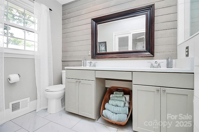 full bath featuring marble finish floor, double vanity, visible vents, toilet, and wooden walls