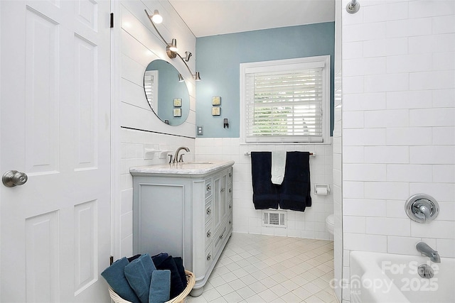 full bathroom with toilet, vanity, visible vents, tile walls, and tile patterned floors