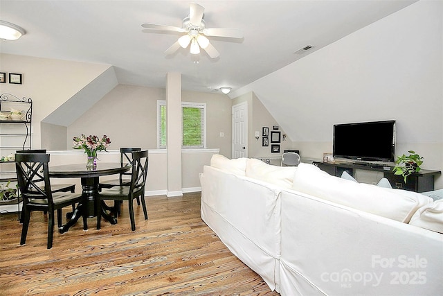 living area featuring ceiling fan, wood finished floors, visible vents, baseboards, and vaulted ceiling