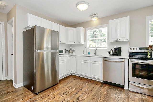 kitchen featuring visible vents, appliances with stainless steel finishes, white cabinetry, a sink, and wood finished floors