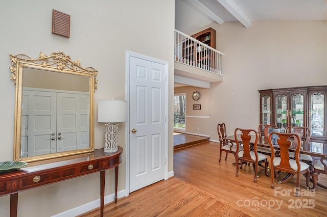 interior space with light wood-type flooring, baseboards, high vaulted ceiling, and beamed ceiling