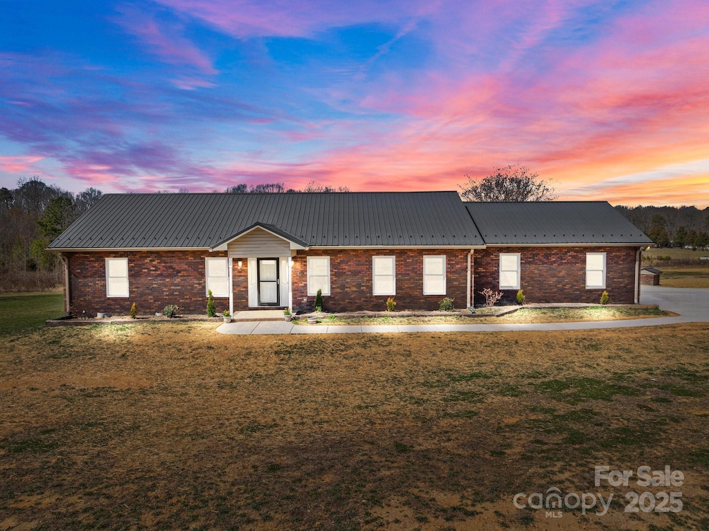 view of front of home with a yard, brick siding, and metal roof