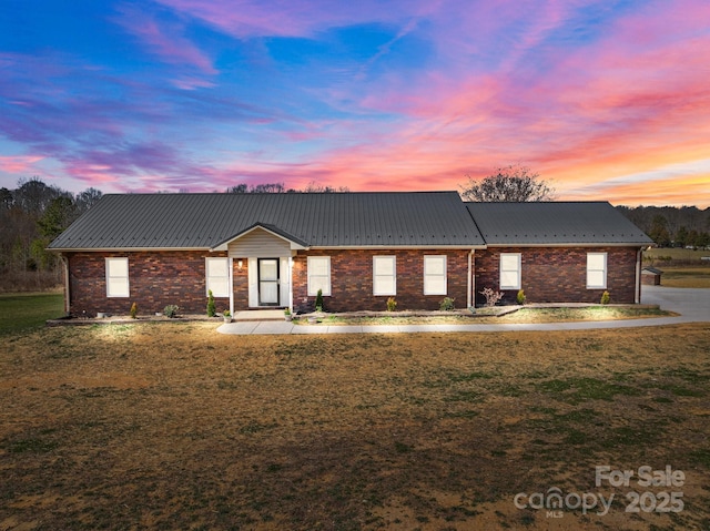 view of front of home with a yard, brick siding, and metal roof