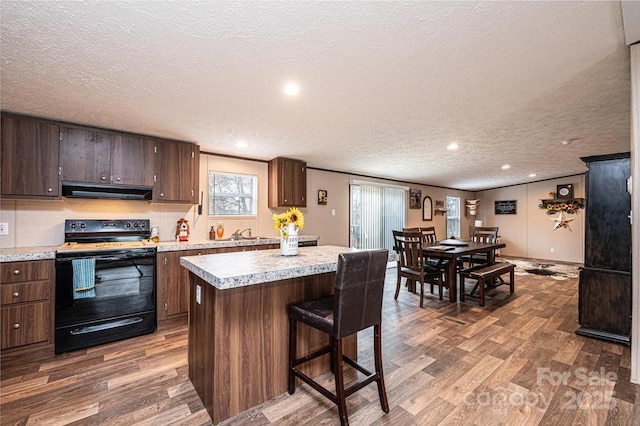 kitchen featuring under cabinet range hood, light countertops, black range with electric stovetop, and wood finished floors