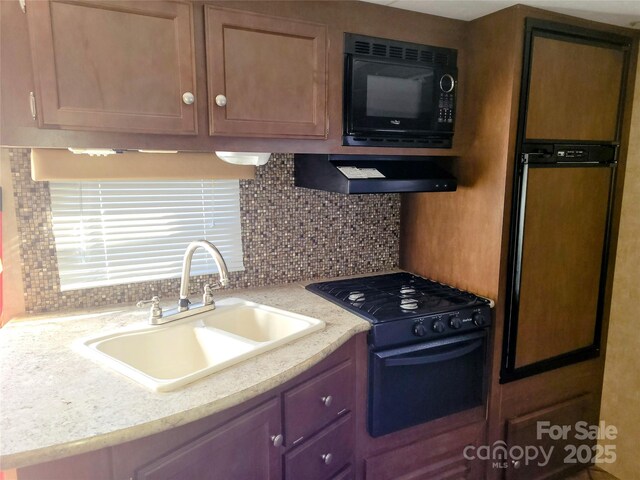 kitchen with black appliances, backsplash, under cabinet range hood, and a sink