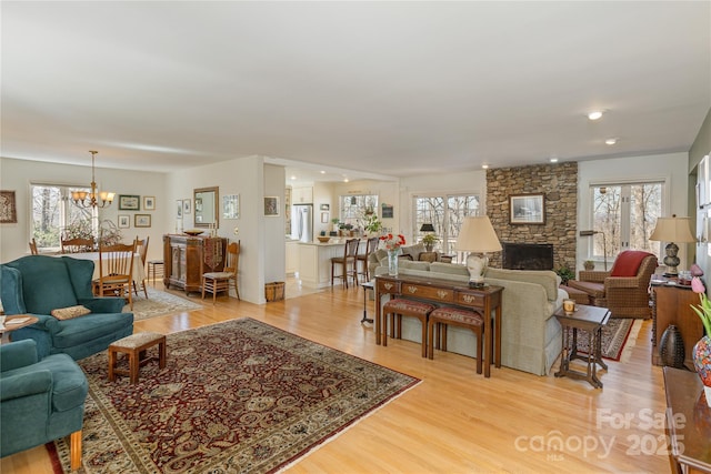 living area featuring a chandelier, a stone fireplace, plenty of natural light, and light wood-style flooring