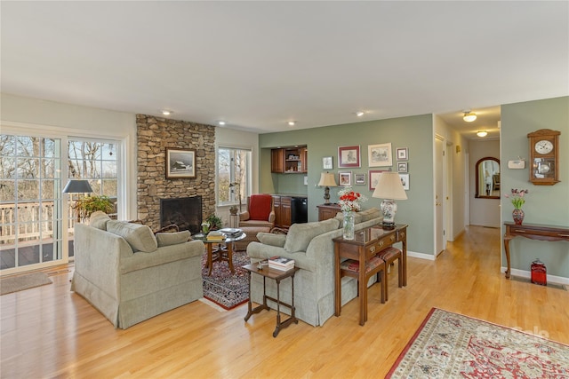 living area with baseboards, a stone fireplace, and light wood-style floors