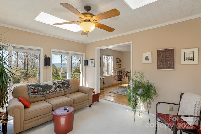 living room with a skylight, baseboards, a ceiling fan, and crown molding