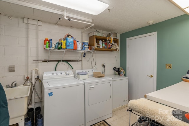 laundry area with light tile patterned flooring, laundry area, a sink, washing machine and clothes dryer, and concrete block wall