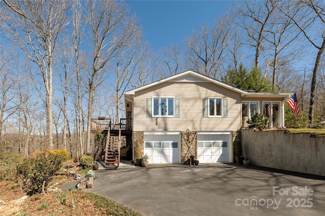 view of front of home with driveway, stone siding, an attached garage, and stairway