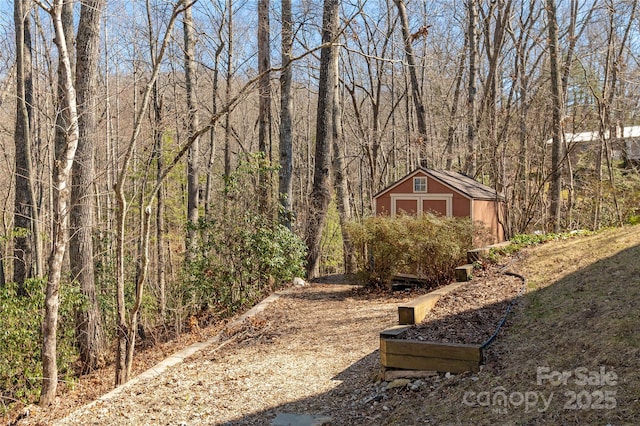 view of yard featuring an outbuilding, a detached garage, a view of trees, and a shed