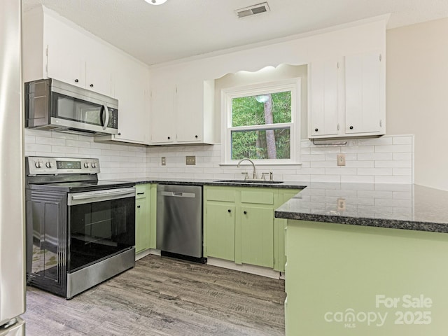 kitchen featuring stainless steel appliances, a peninsula, wood finished floors, a sink, and visible vents