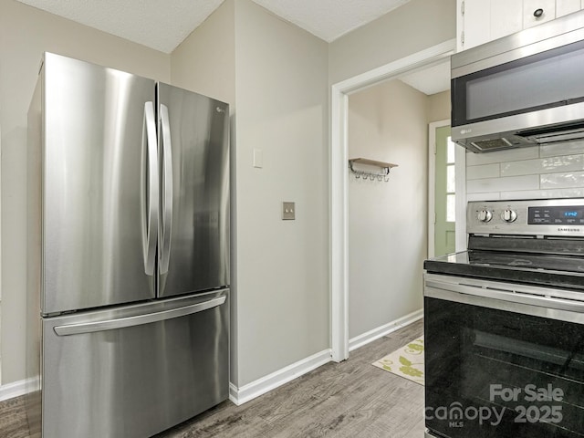 kitchen with stainless steel appliances, white cabinets, baseboards, and wood finished floors