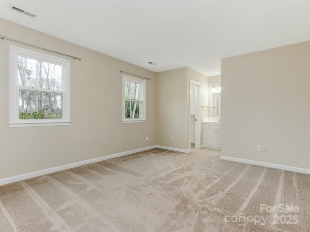 unfurnished room with baseboards, visible vents, a textured ceiling, and light colored carpet