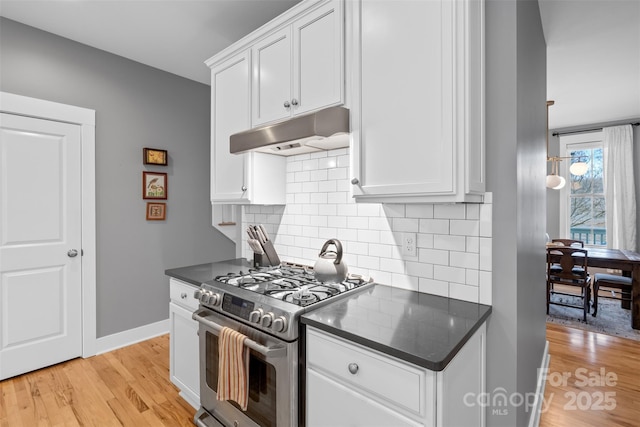 kitchen with under cabinet range hood, stainless steel gas stove, dark countertops, and light wood finished floors