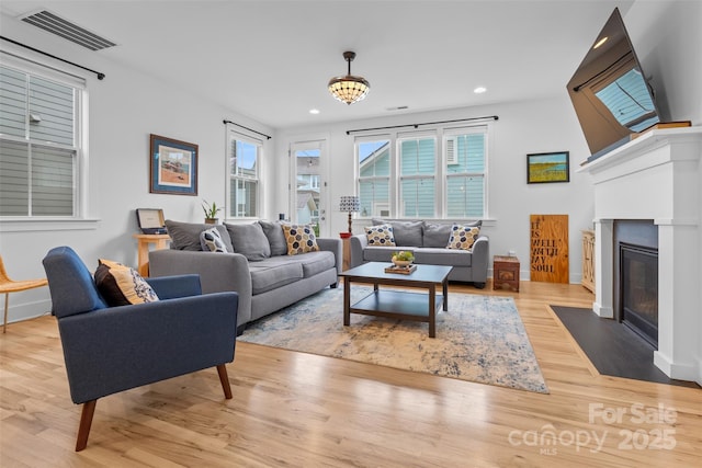 living area with light wood finished floors, visible vents, a healthy amount of sunlight, and a fireplace with flush hearth