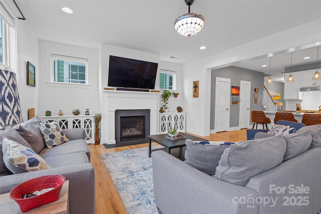 living room with recessed lighting, a fireplace with flush hearth, light wood-style flooring, and stairs