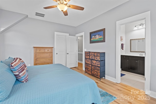 bedroom with a ceiling fan, baseboards, visible vents, ensuite bathroom, and light wood-type flooring