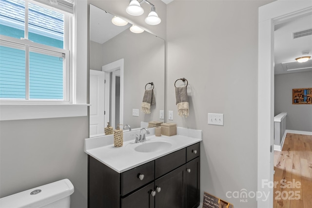 bathroom featuring visible vents, baseboards, toilet, wood finished floors, and vanity