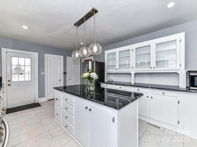 kitchen with dark stone countertops, visible vents, freestanding refrigerator, white cabinets, and a center island