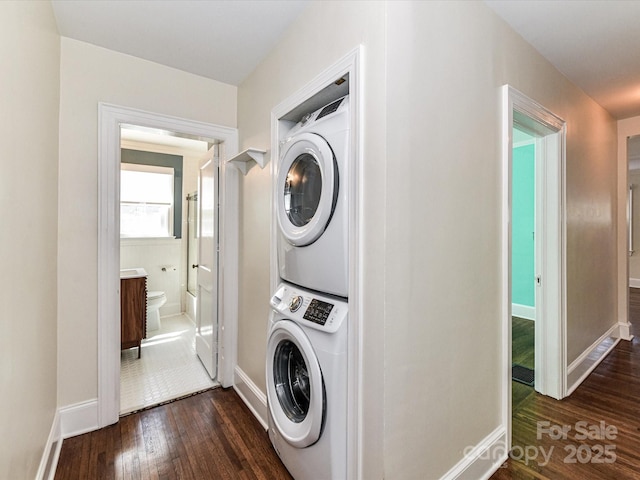 clothes washing area with laundry area, dark wood-style floors, stacked washer and clothes dryer, and baseboards