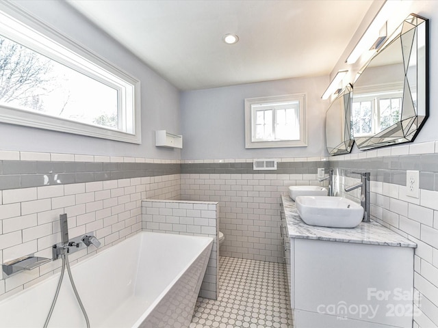 bathroom featuring toilet, double vanity, a bathtub, tile walls, and a sink