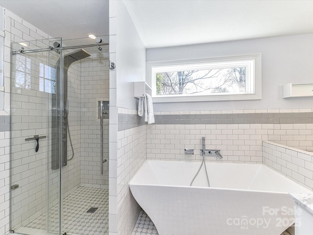 full bathroom featuring a soaking tub, wainscoting, a stall shower, and tile walls