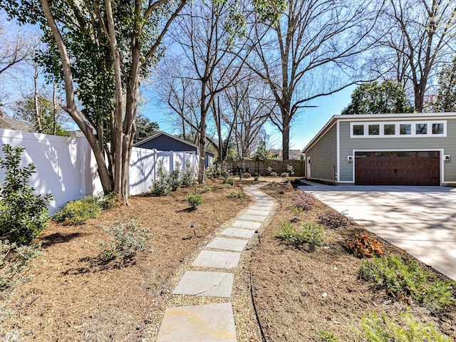 view of yard with an outbuilding, concrete driveway, a garage, and fence