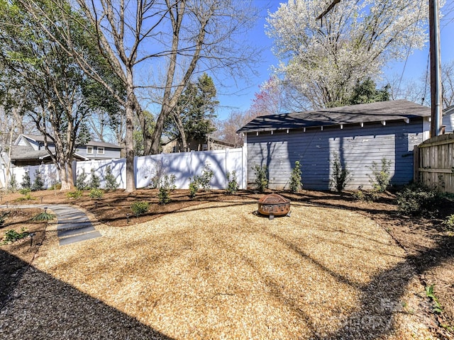 view of yard with an outdoor structure, a fenced backyard, and an outdoor fire pit