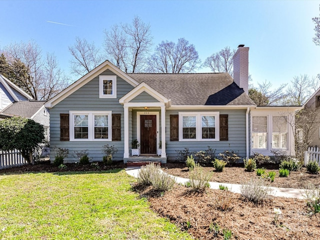 view of front of house featuring a front lawn, a shingled roof, a chimney, and fence