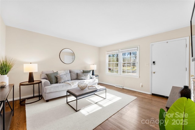 living room featuring visible vents, baseboards, and wood finished floors