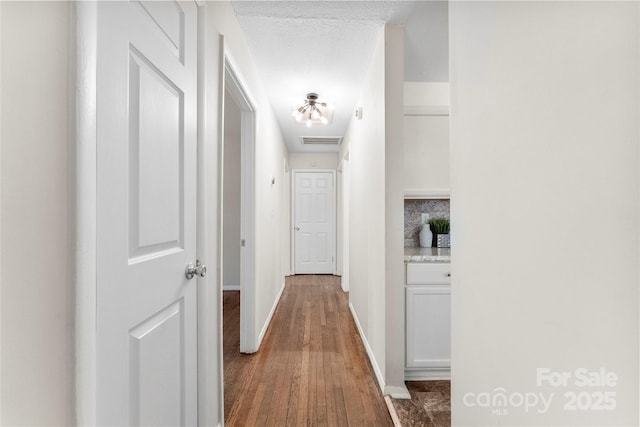 hall with dark wood finished floors, baseboards, visible vents, and a textured ceiling