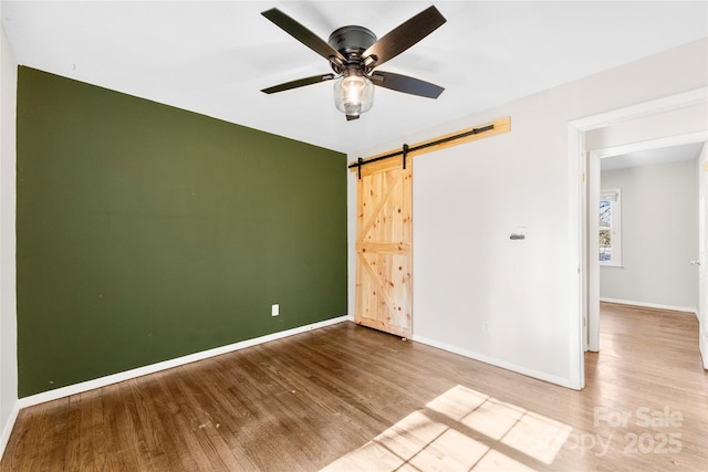 empty room featuring baseboards, a ceiling fan, a barn door, and wood finished floors