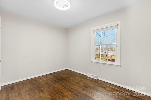 spare room featuring visible vents, dark wood-type flooring, and baseboards