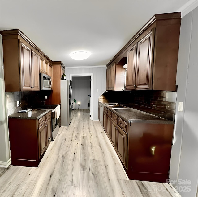 kitchen featuring light wood-style flooring, a sink, appliances with stainless steel finishes, decorative backsplash, and dark countertops