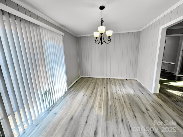 unfurnished dining area featuring a notable chandelier, hardwood / wood-style floors, baseboards, and crown molding