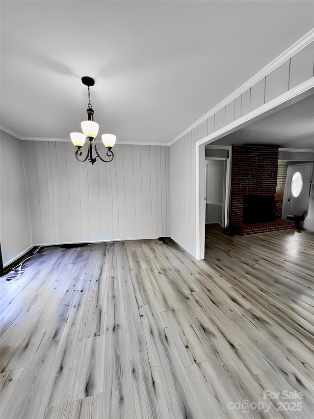 unfurnished dining area with a brick fireplace, a notable chandelier, crown molding, and wood finished floors