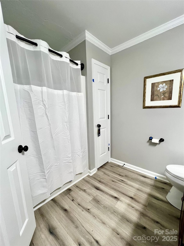 bathroom featuring baseboards, a shower with shower curtain, toilet, ornamental molding, and wood finished floors